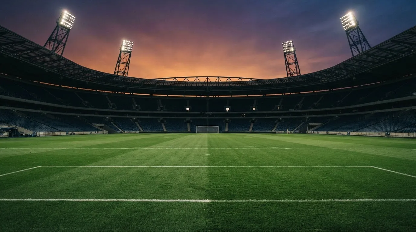 An empty football stadium with floodlight masts at dusk