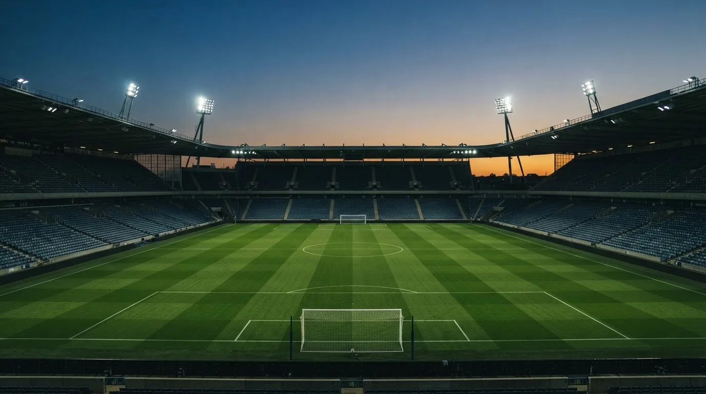 An empty football stadium with floodlight masts at dusk