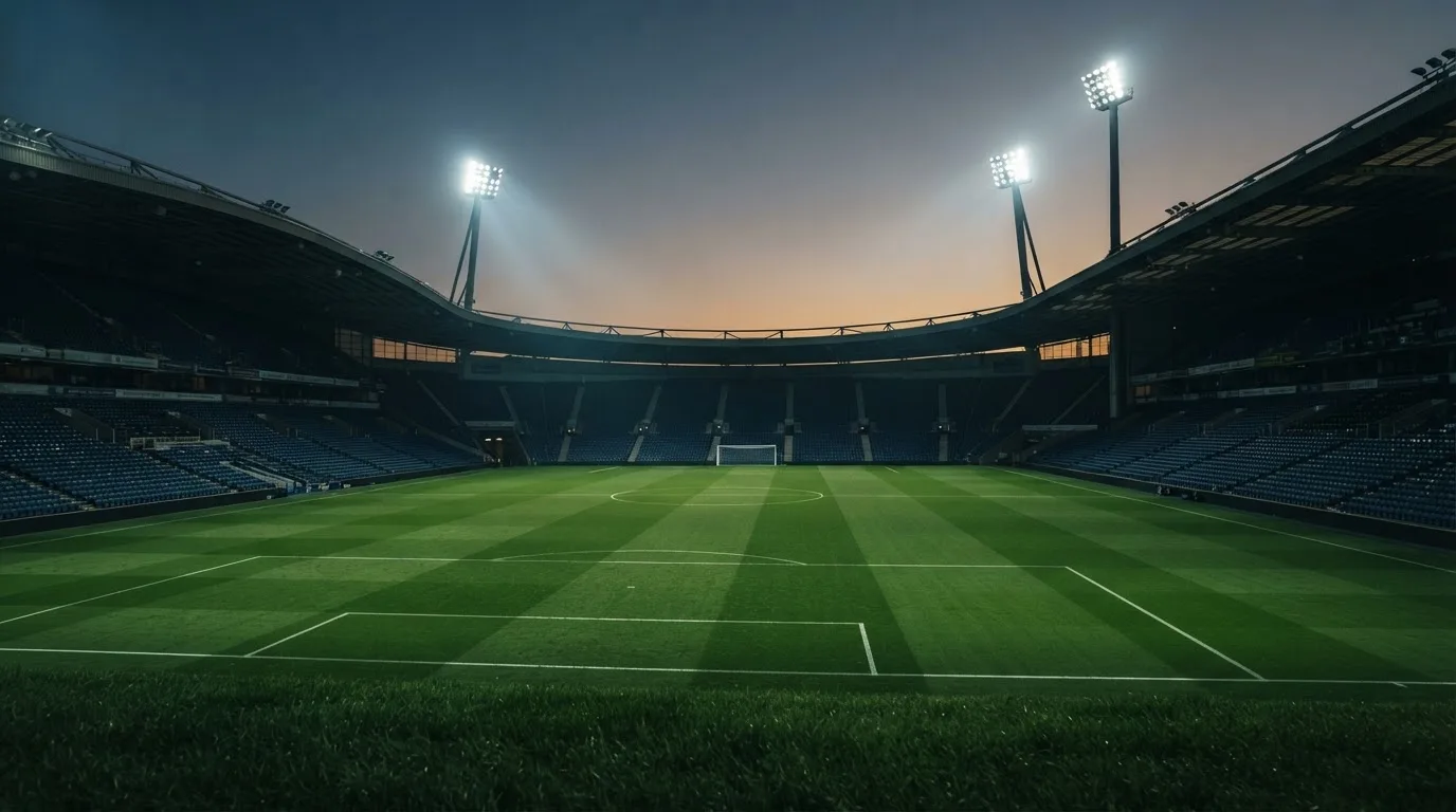An empty football stadium with floodlight masts at dusk