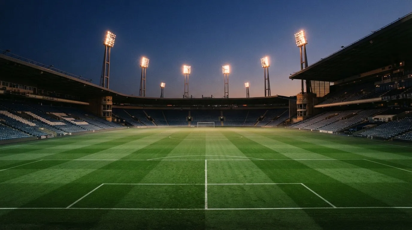 An empty football stadium with floodlight masts at dusk