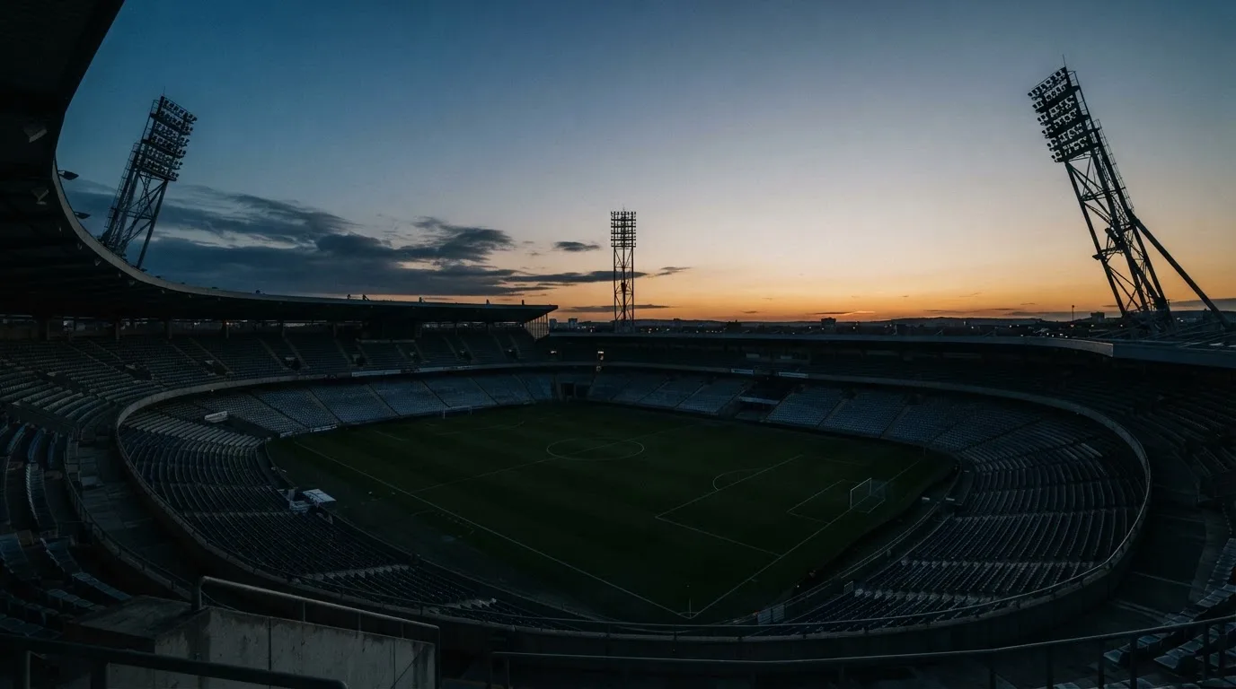 An empty football stadium with floodlight masts at dusk