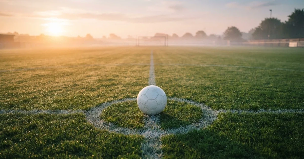 A ball on the centre spot of a grass pitch in morning light