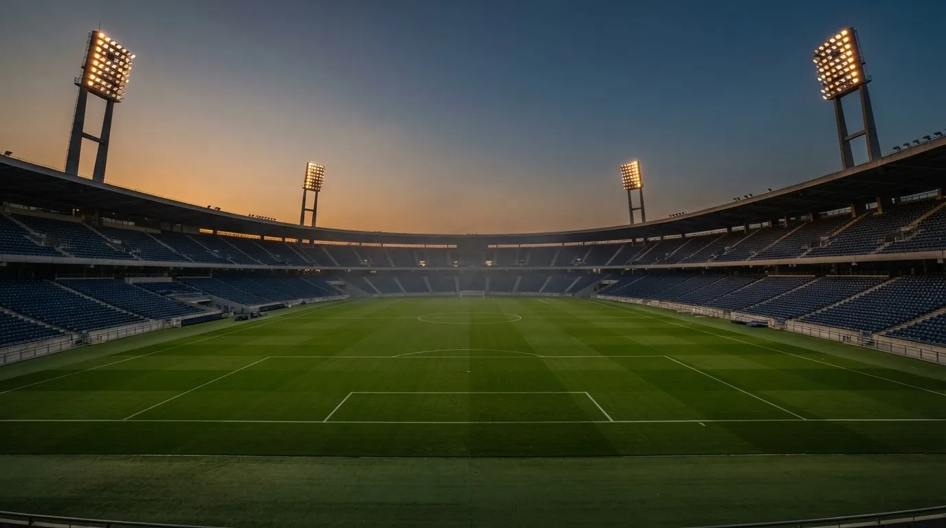 An empty football stadium with floodlight masts at dusk