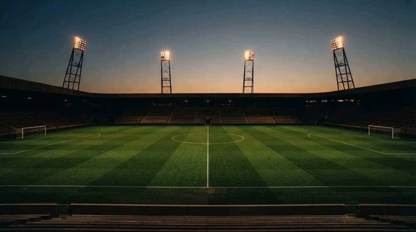 An empty football stadium with floodlight masts at dusk